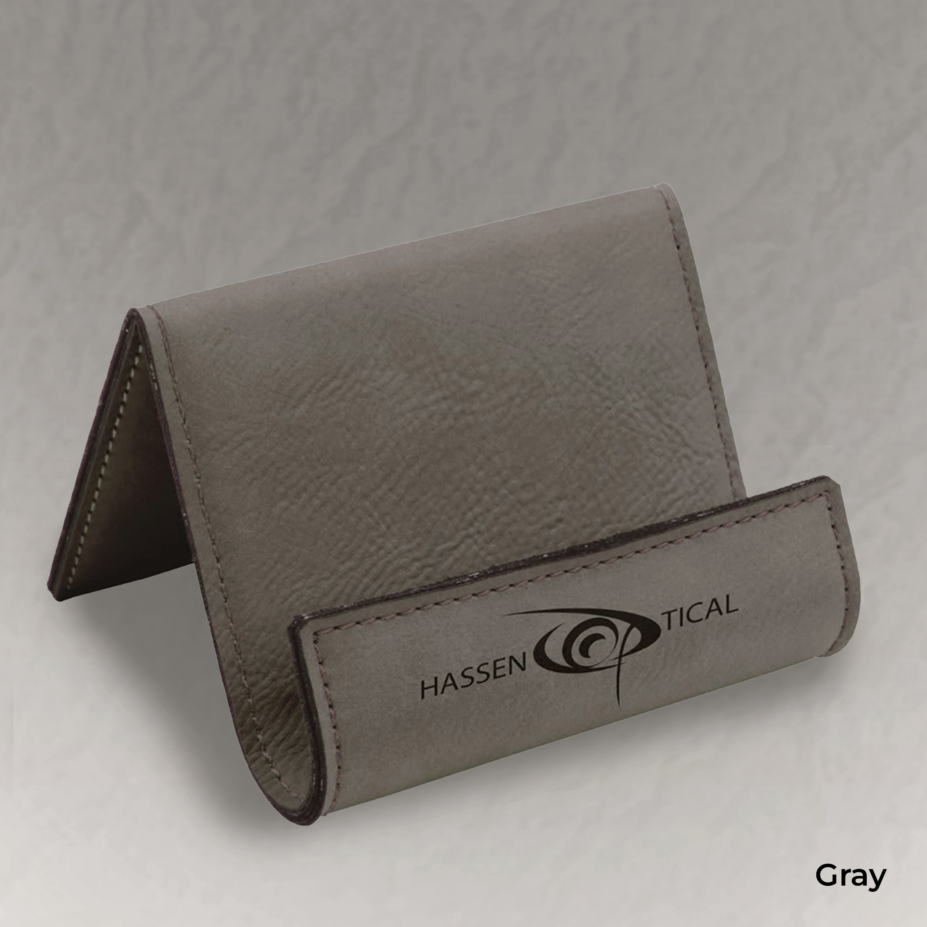 Gray leather business card holder with 'Hassen Optical' branding on a light gray background