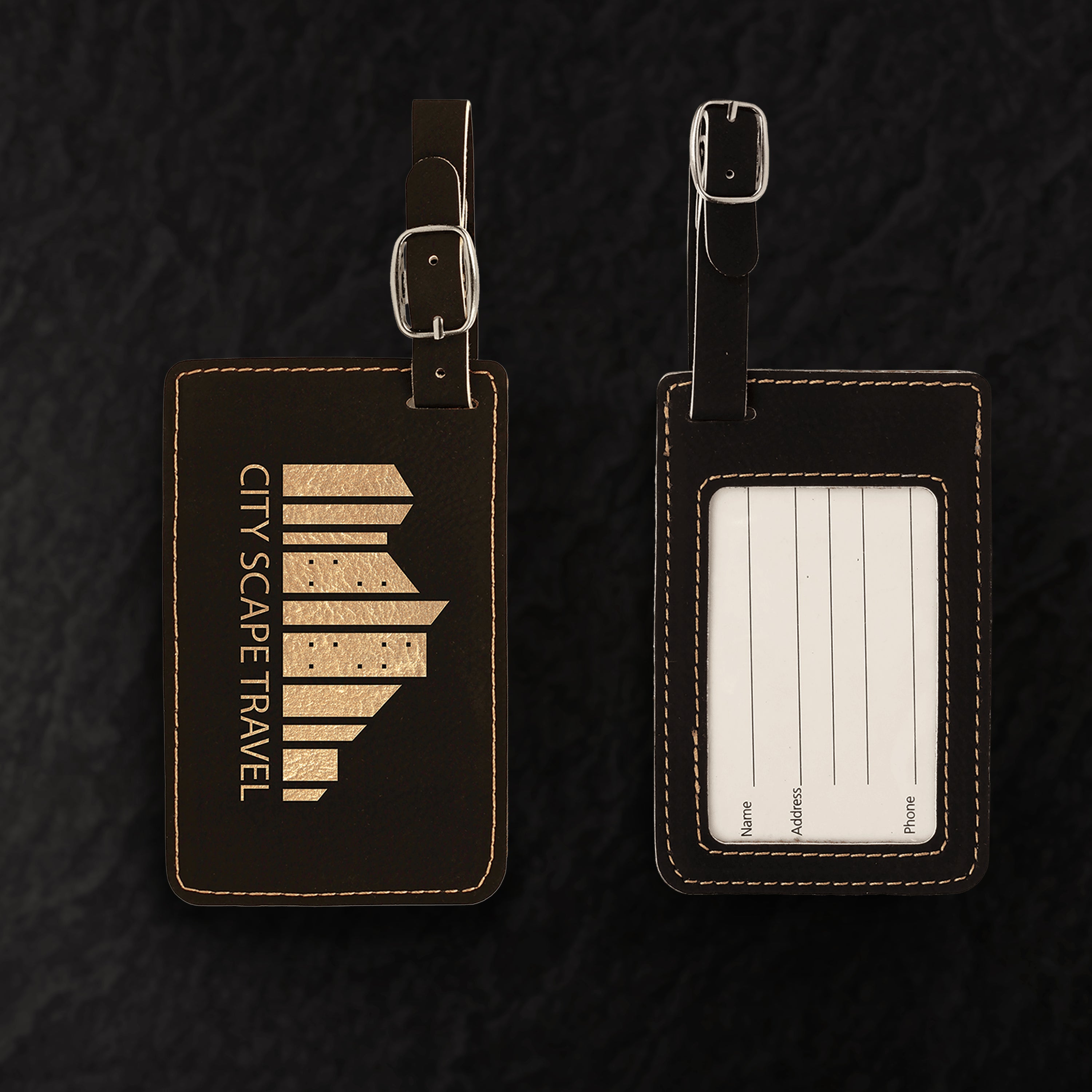 Two black leather luggage tags with one featuring a map design and the other with a label area on a dark textured background.