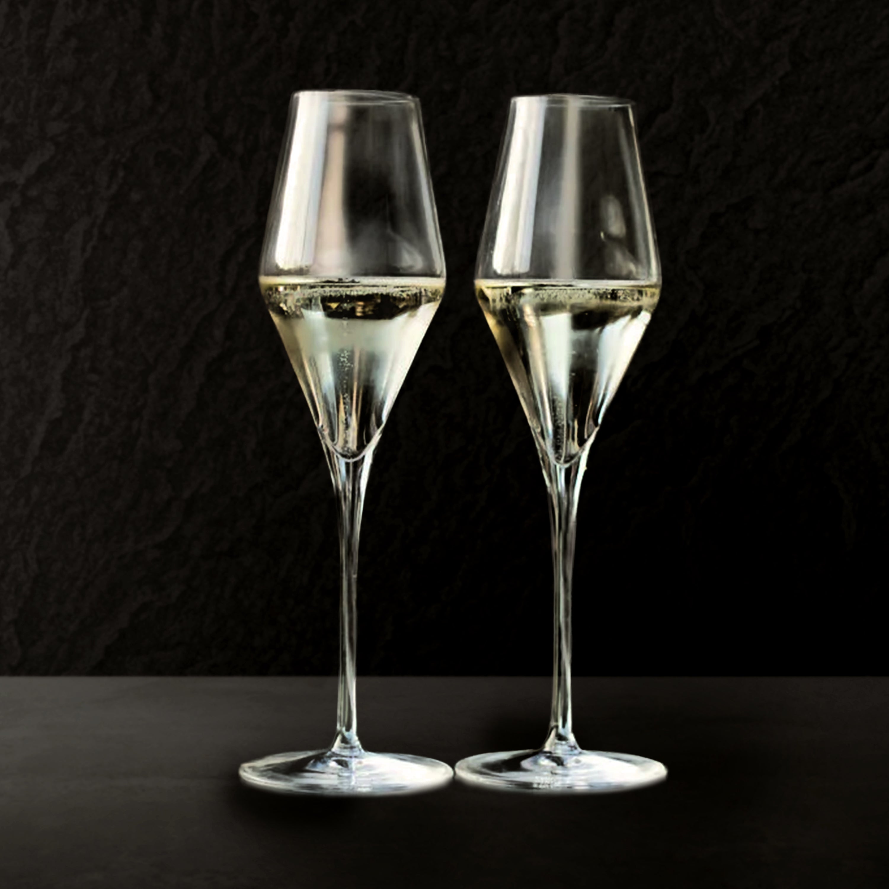 Two champagne glasses filled with champagne on a black background