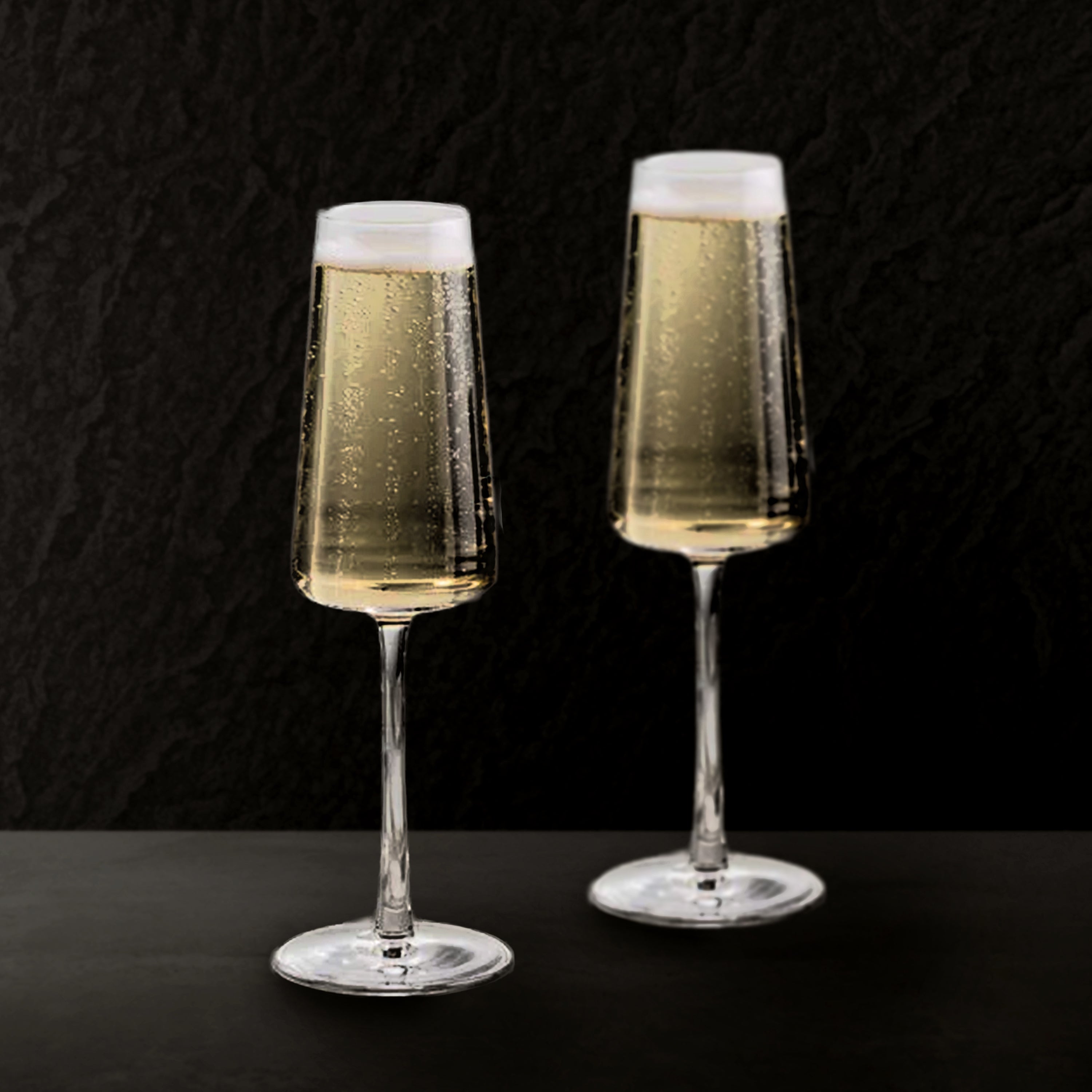 Two champagne flutes filled with sparkling wine on a black background