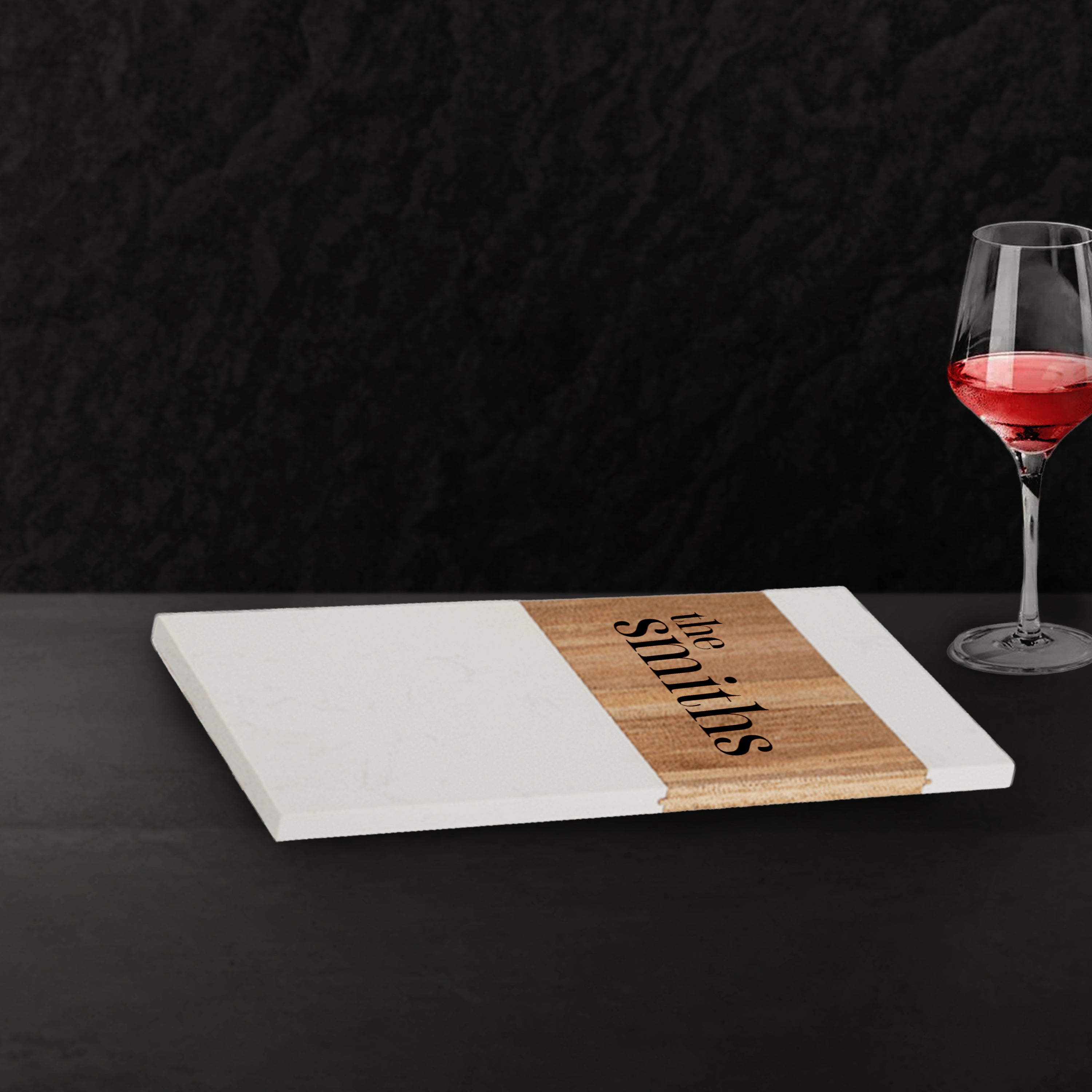 Personalized cutting board with 'the smiths' engraving on a dark surface with a glass of red wine.