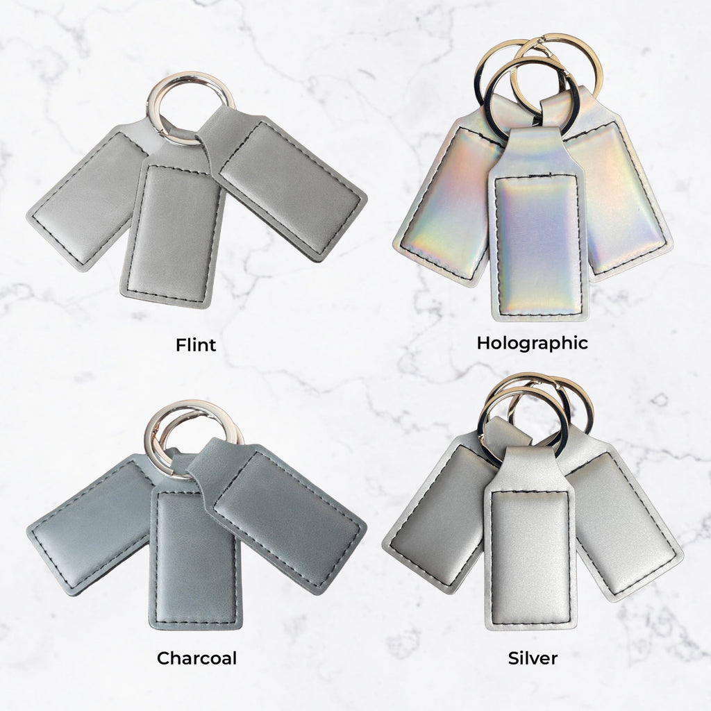 Keychains in Flint, Holographic, Charcoal, and Silver on a textured white background