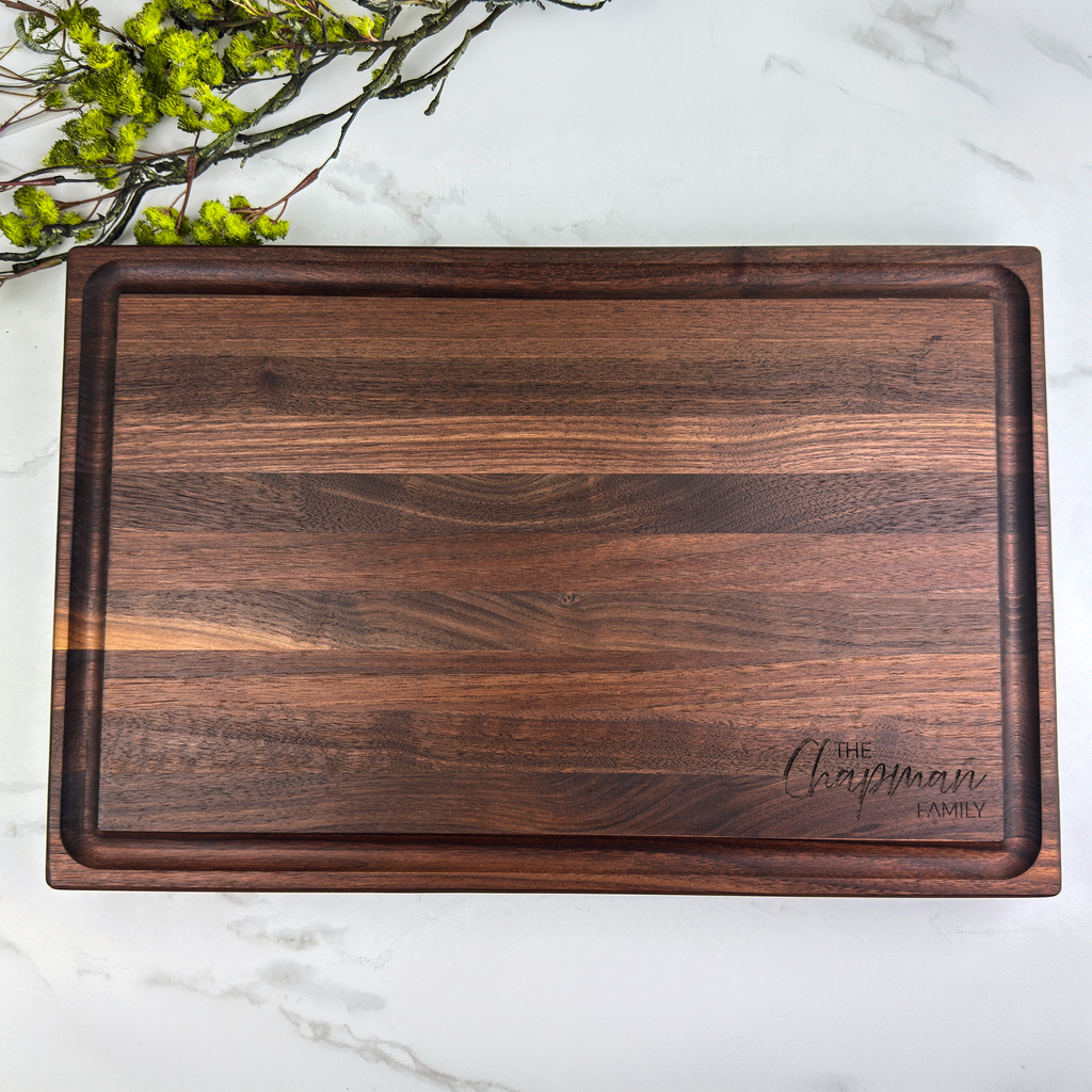 Wooden cutting board with 'The Chapman Family' engraving on a marble surface with greenery.