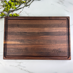 Wooden cutting board with 'The Chapman Family' engraving on a marble surface with greenery.