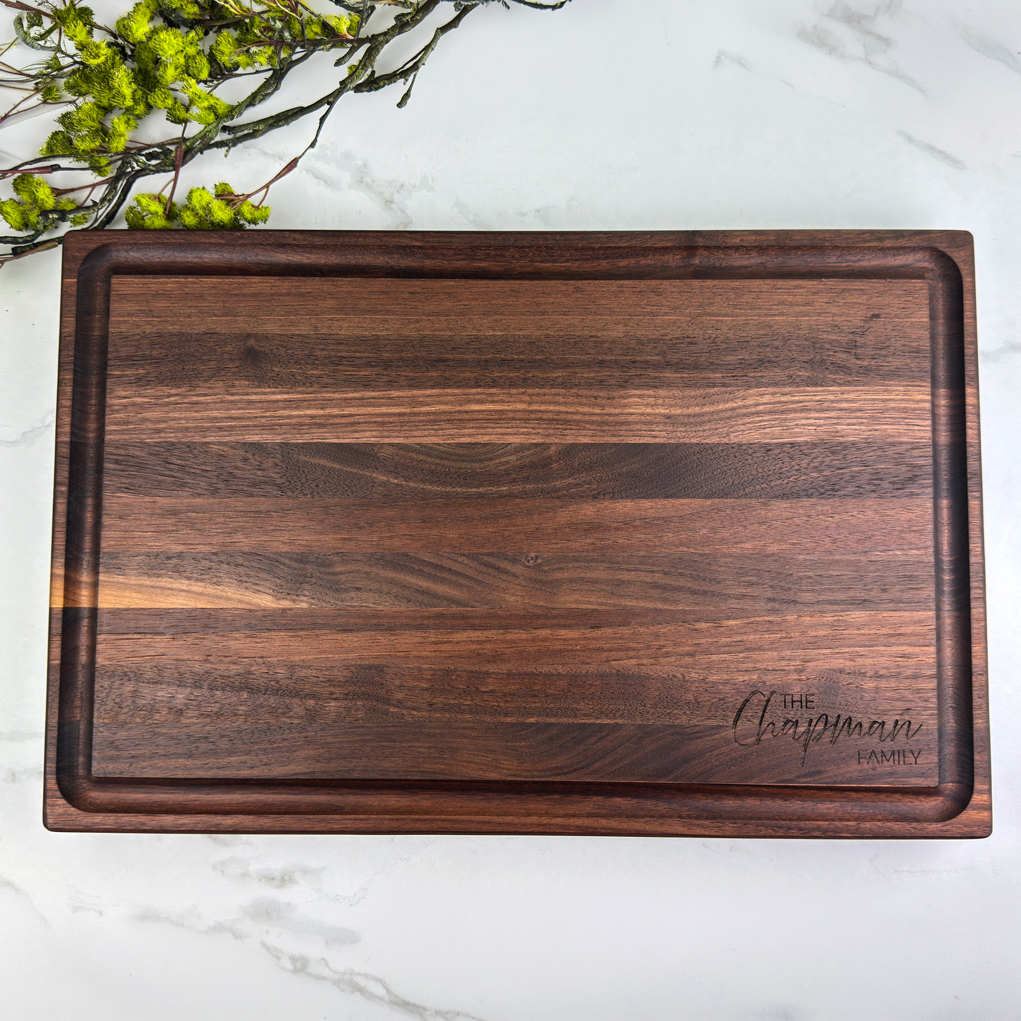 Wooden cutting board with 'The Chapman Family' engraving on a marble surface with greenery.